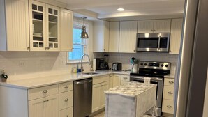 A modern kitchen with light-colored cabinets, stainless steel appliances, and a marble countertop. - Spectacular Ocean Sunsets I Pet Friendly (Weymouth)