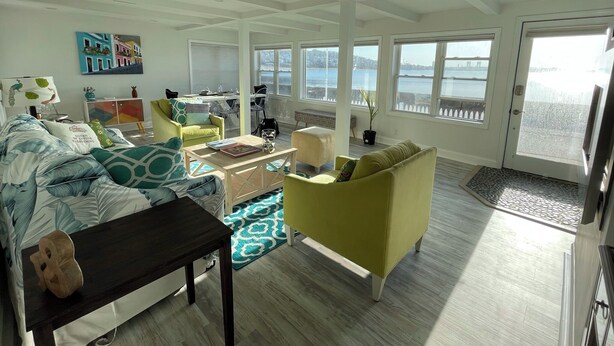 A spacious living room with a large window overlooking a body of water, a dining area with a view, and a cozy seating arrangement. - Spectacular Ocean Sunsets I Pet Friendly (Weymouth)