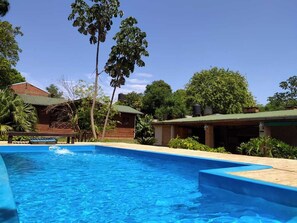 Une piscine à l’eau d’un bleu cristallin, entourée d’une végétation luxuriante et de bâtiments en bois.