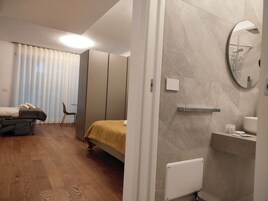 A bedroom with a bed, a chair, a massage table, and a bathroom with a toilet, sink, and mirror.