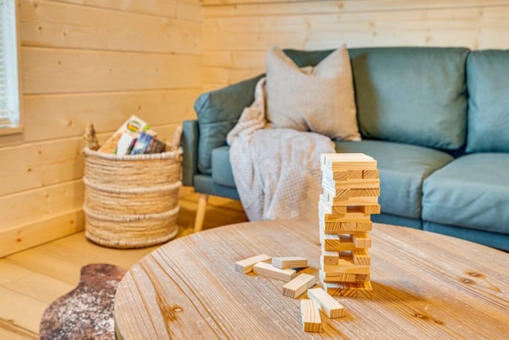 A wooden cabin interior with a round wooden table, a woven basket, and a green sofa with a cushion.