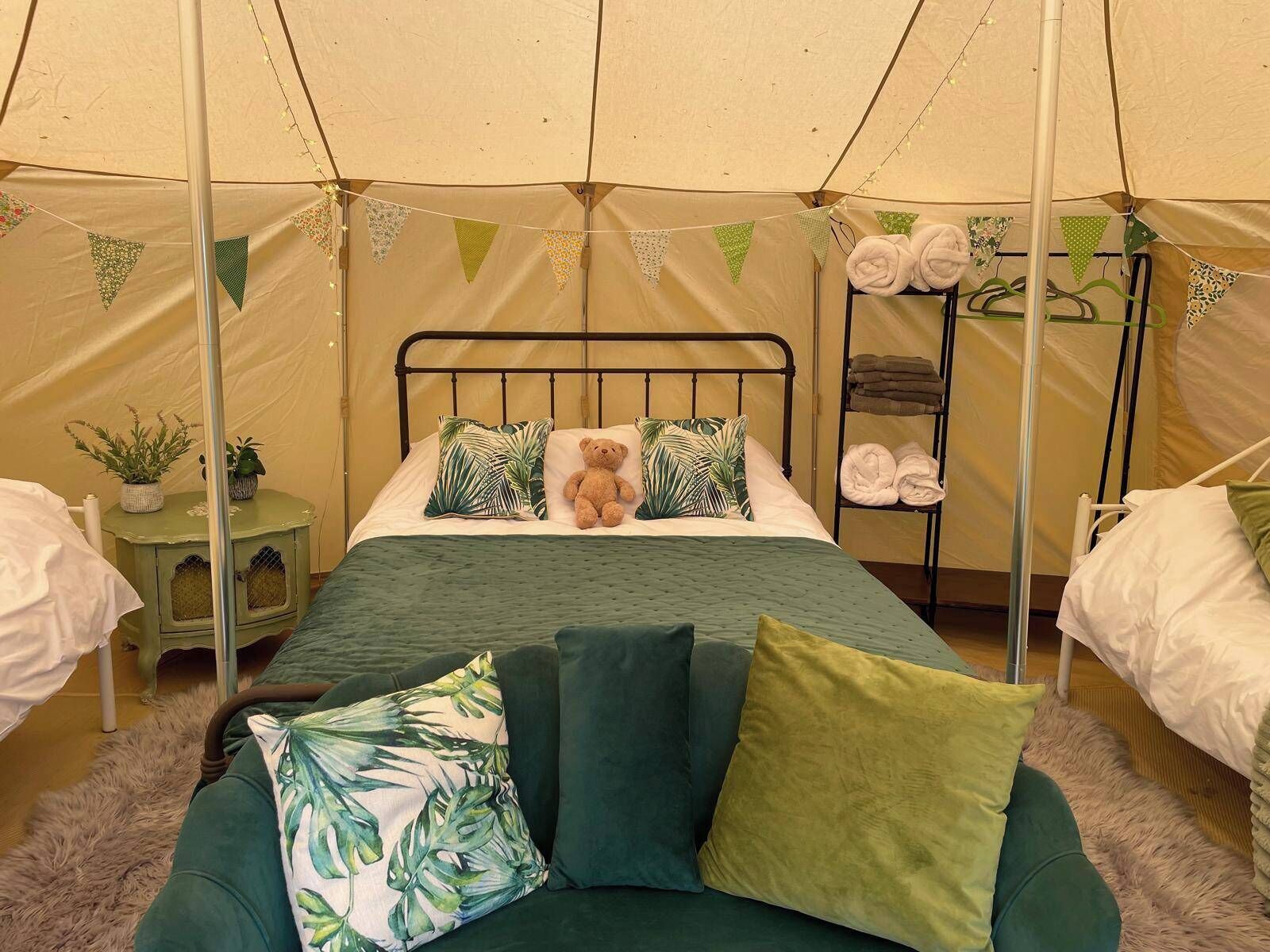 A cozy tented room with a bed, a green sofa, and a shelf with towels.