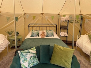 Een gezellige tentkamer met een bed, een groene bank en een plank met handdoeken.