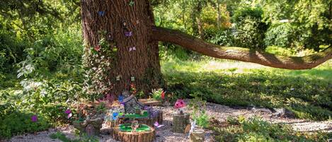 A tree with a wooden swing hanging from its branches, surrounded by a garden with various plants and a small pond.