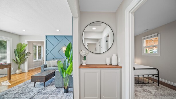 A modern living room with a sofa, coffee table, and a large plant. There is a wooden cabinet with a mirror above it and a bed with a metal frame in the corner. - PDX Stay w/BBQ, Firepit & Pool Table (Portland)