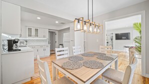 A modern kitchen with white cabinets, a wooden dining table with four chairs, and a hanging light fixture. - PDX Stay w/BBQ, Firepit & Pool Table (Portland)
