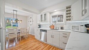 A modern kitchen with white cabinets, stainless steel appliances, and a wooden dining area. - PDX Stay w/BBQ, Firepit & Pool Table (Portland)