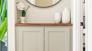 A hallway with a wooden counter, a white cabinet, a round mirror, and a potted plant. - PDX Stay w/BBQ, Firepit & Pool Table (Portland)