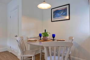 A dining area with a white table, chairs, a framed picture, and a hanging light fixture. - Cottage in Grantley Near Fountains Abbey (Ripon)