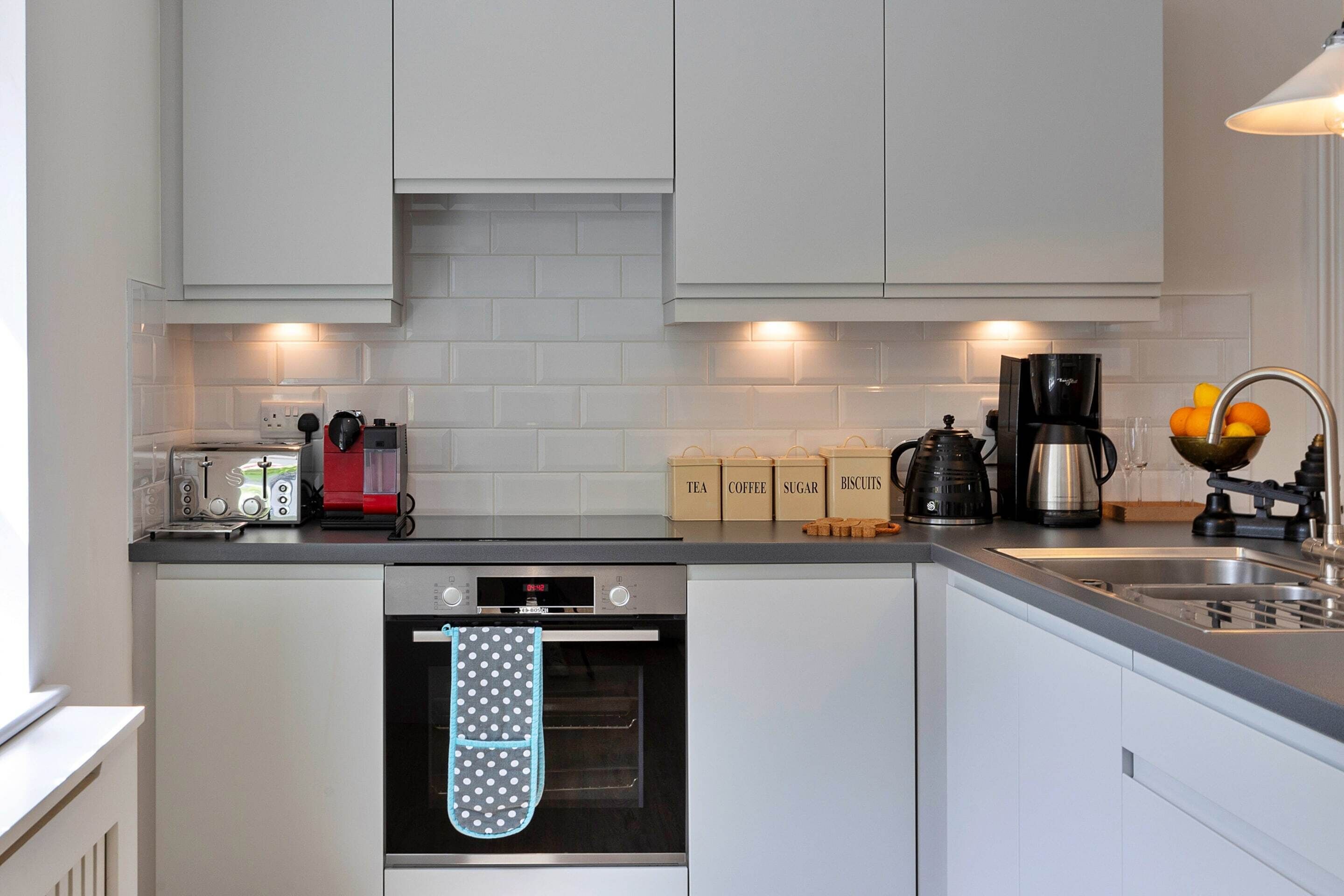 A modern kitchen with white cabinetry, a built-in oven, a coffee maker, and a fruit bowl.