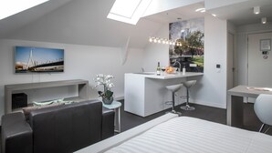Una camera d'albergo moderna con un letto, un divano, un angolo cottura con un bancone, un tavolo da pranzo e un'ampia finestra con vista sulla città.