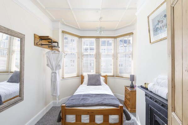 Een slaapkamer met een bed, een houten dressoir, een open haard, een raam met jaloezieën, een badjas en een spiegel.