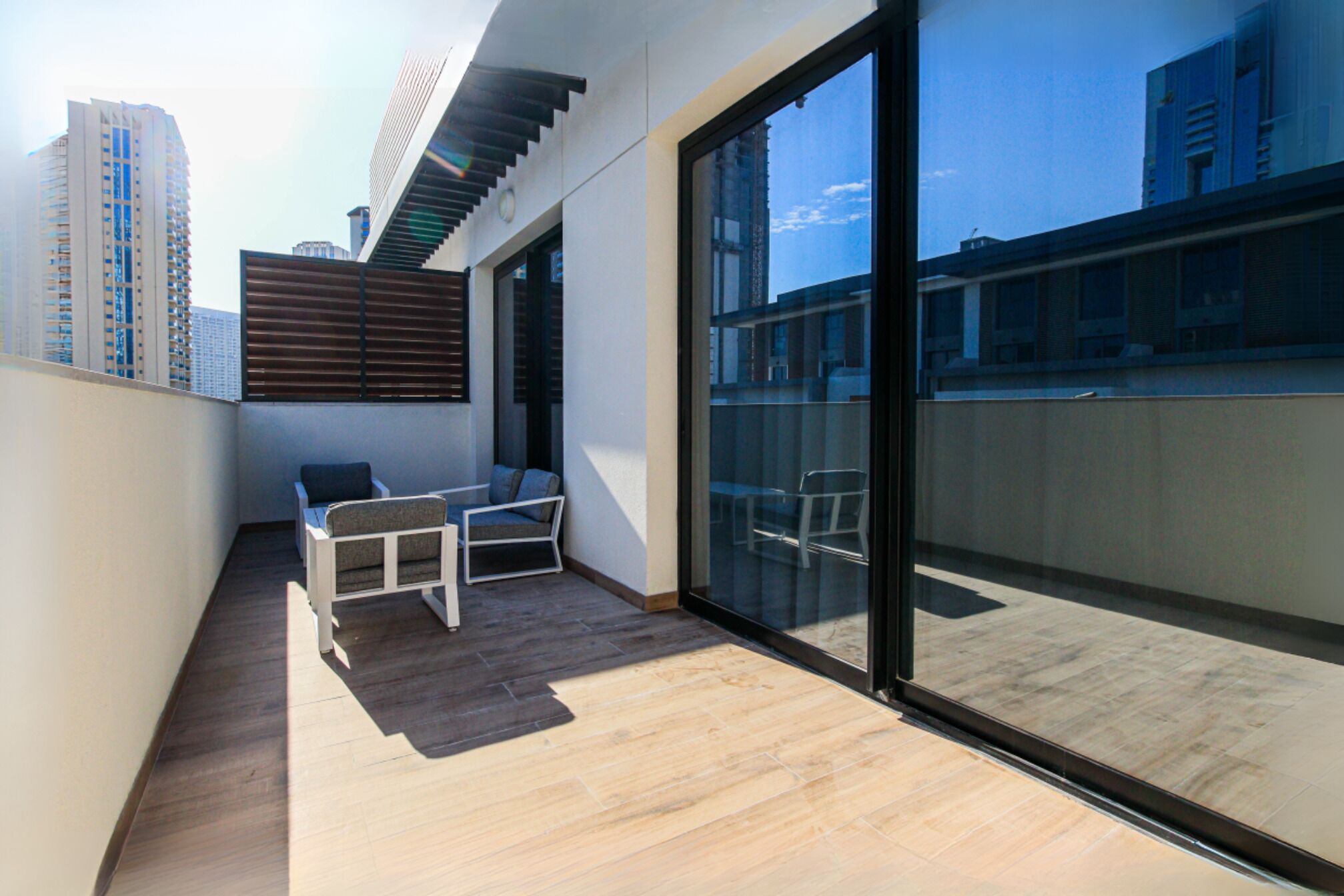 Un balcón con dos sillas, piso de madera y un gran ventanal que da a un espacio exterior.