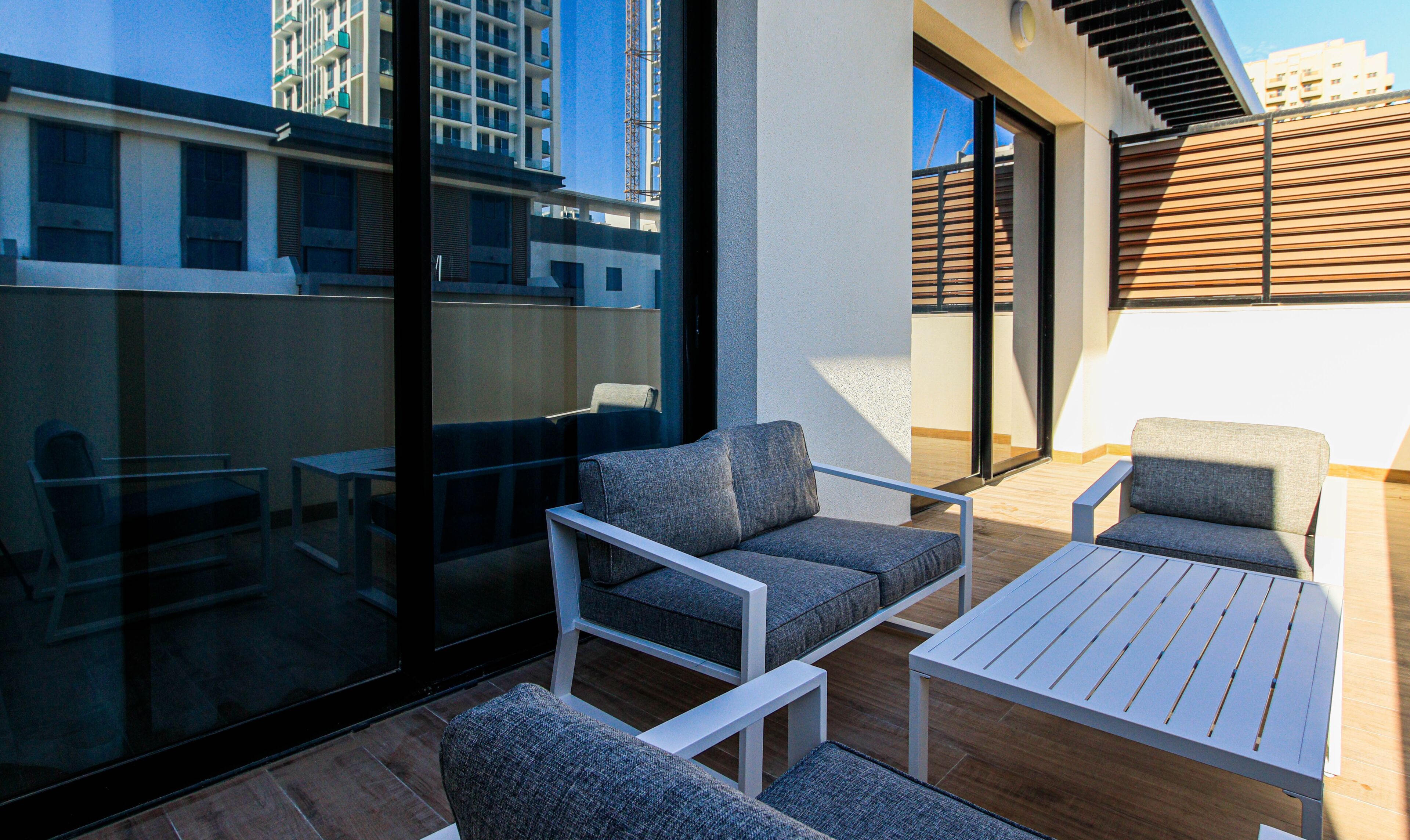 A modern outdoor seating area with a glass wall, a wooden deck, and a view of a high-rise building.