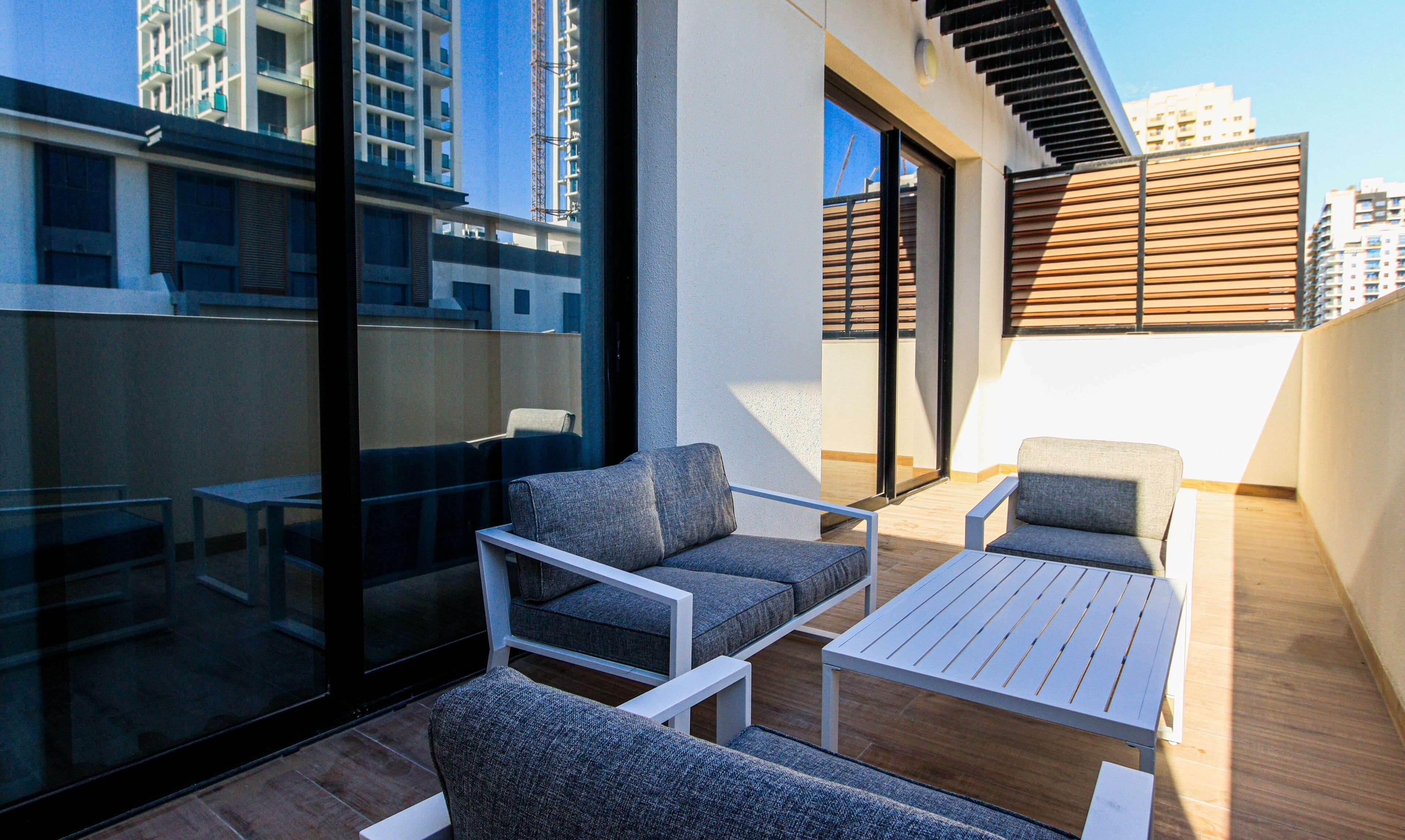 A modern outdoor seating area with a glass wall, wooden deck, and a view of high-rise buildings.