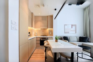 Una cocina moderna con electrodomésticos integrados, un comedor con mesa y sillas, y una sala de estar con sofá y una planta.