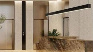A modern hotel lobby with a reception desk, a vertical light fixture, and a balcony. - Modern 1BR Living in Oakley Square (Dubai)