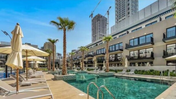 A modern hotel with a pool area, sun loungers, and palm trees. - Modern 1BR Living in Oakley Square (Dubai)