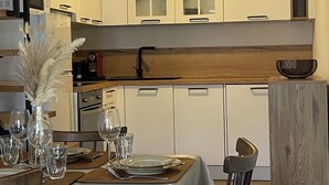 A modern kitchen with white cabinets, a wooden countertop, and a dining area set with a table, chairs, and glassware. - Small village house (Bastelica)