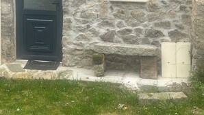 A stone building with a dark door, a small window, and a light fixture. - Small village house (Bastelica)