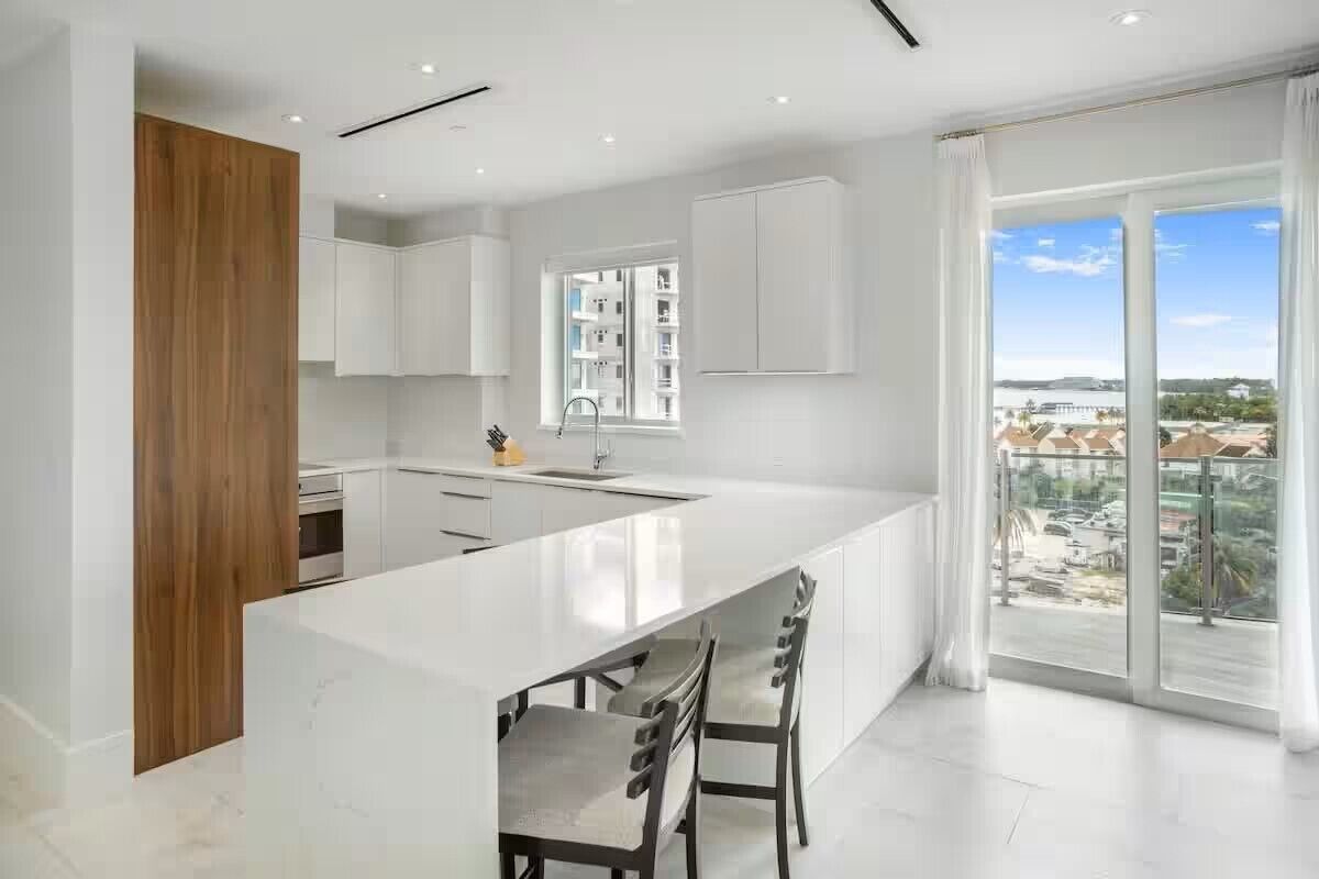 A modern kitchen with a large island, white cabinets, and a view of the city through large windows.