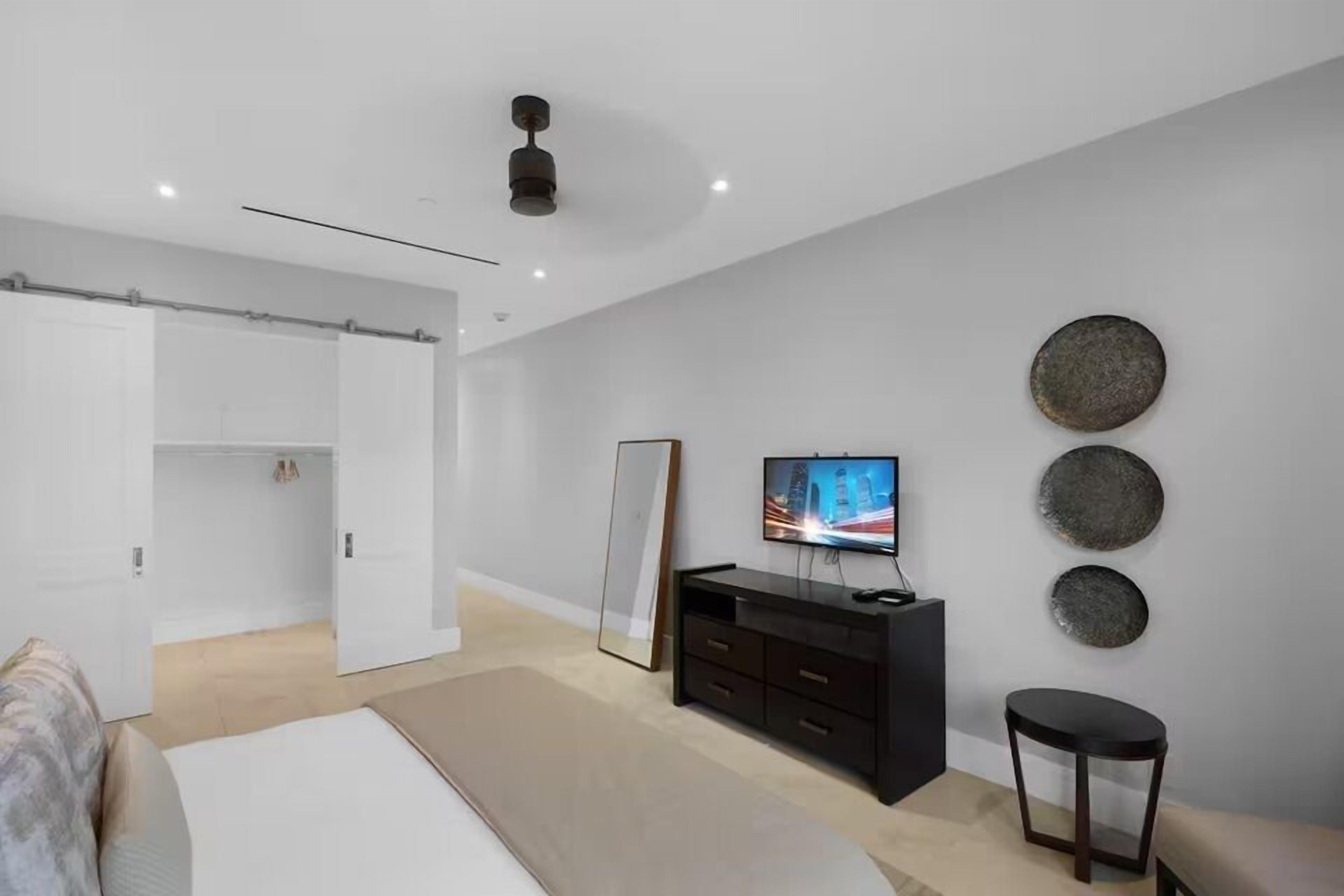A modern bedroom with a bed, a TV, a dresser, and a mirror.