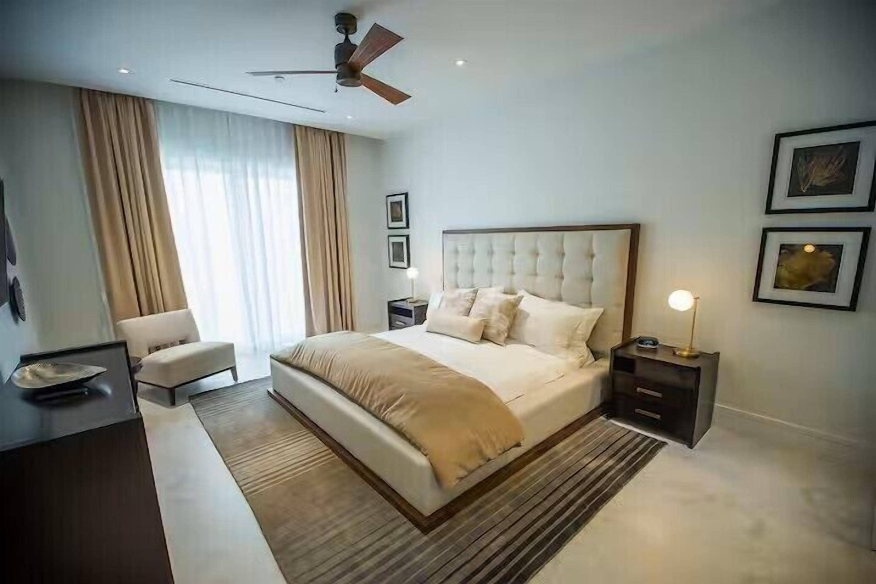 Une chambre à coucher moderne avec un grand lit, un ventilateur de plafond et une table de chevet avec une lampe.