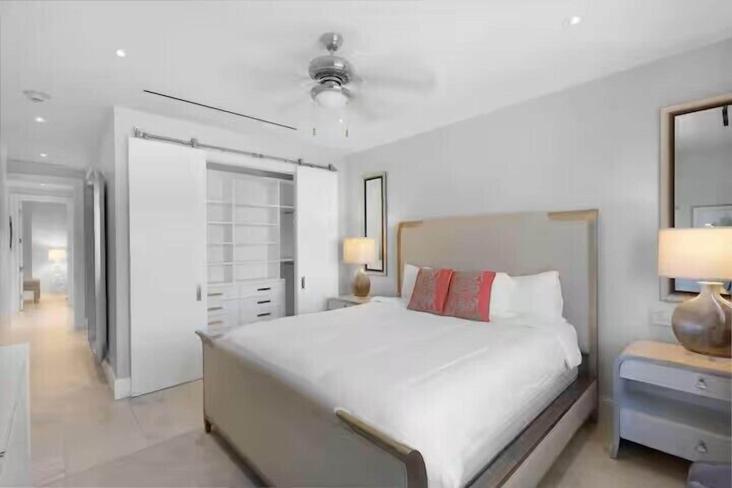 Ein modernes Hotelzimmer mit einem großen Bett, einem Deckenventilator, einem Kleiderschrank und einem Nachttisch mit Lampe.