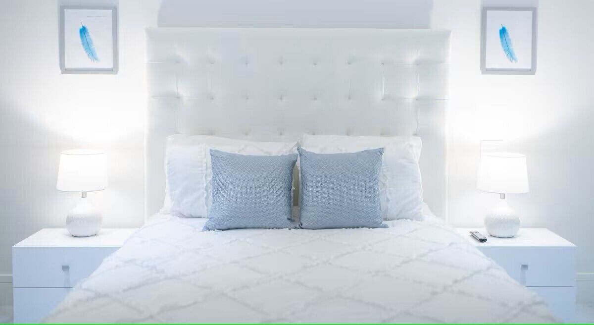 Ein Schlafzimmer mit einer gebügelten Kopfstütze, zwei Nachttischen mit Lampen und einem Bett mit gemustertem Bettbezug.