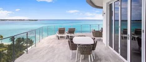 A balcony with a table and chairs, overlooking a clear blue sea and a distant island.