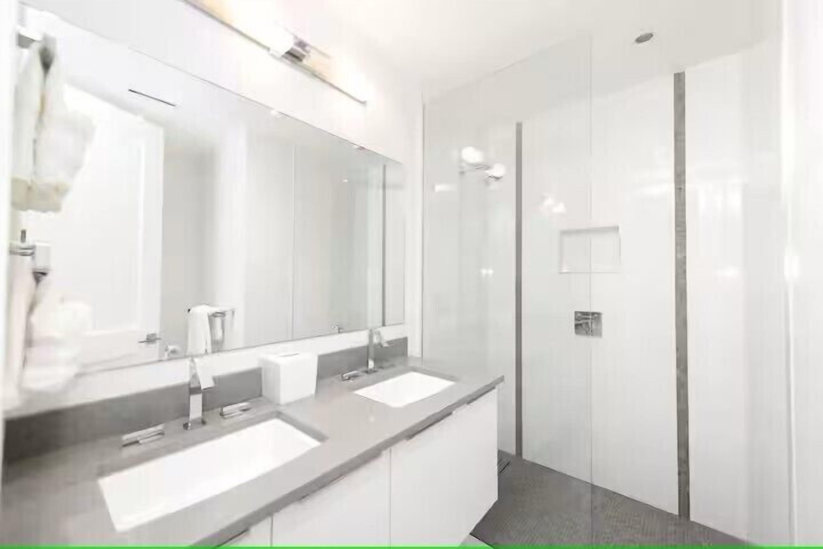 Une salle de bain moderne avec deux lavabos, un grand miroir et un espace douche.