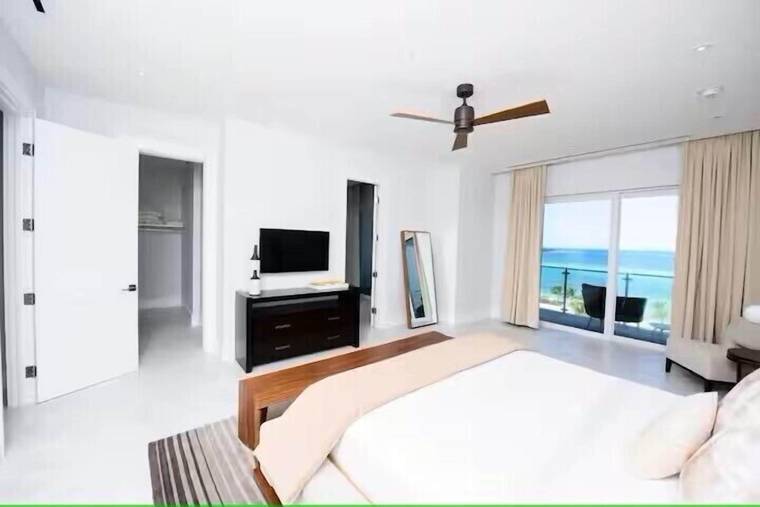 Une chambre moderne dotée d’un grand lit, d’une télévision, d’un ventilateur de plafond et d’un balcon offrant une vue sur l’océan.