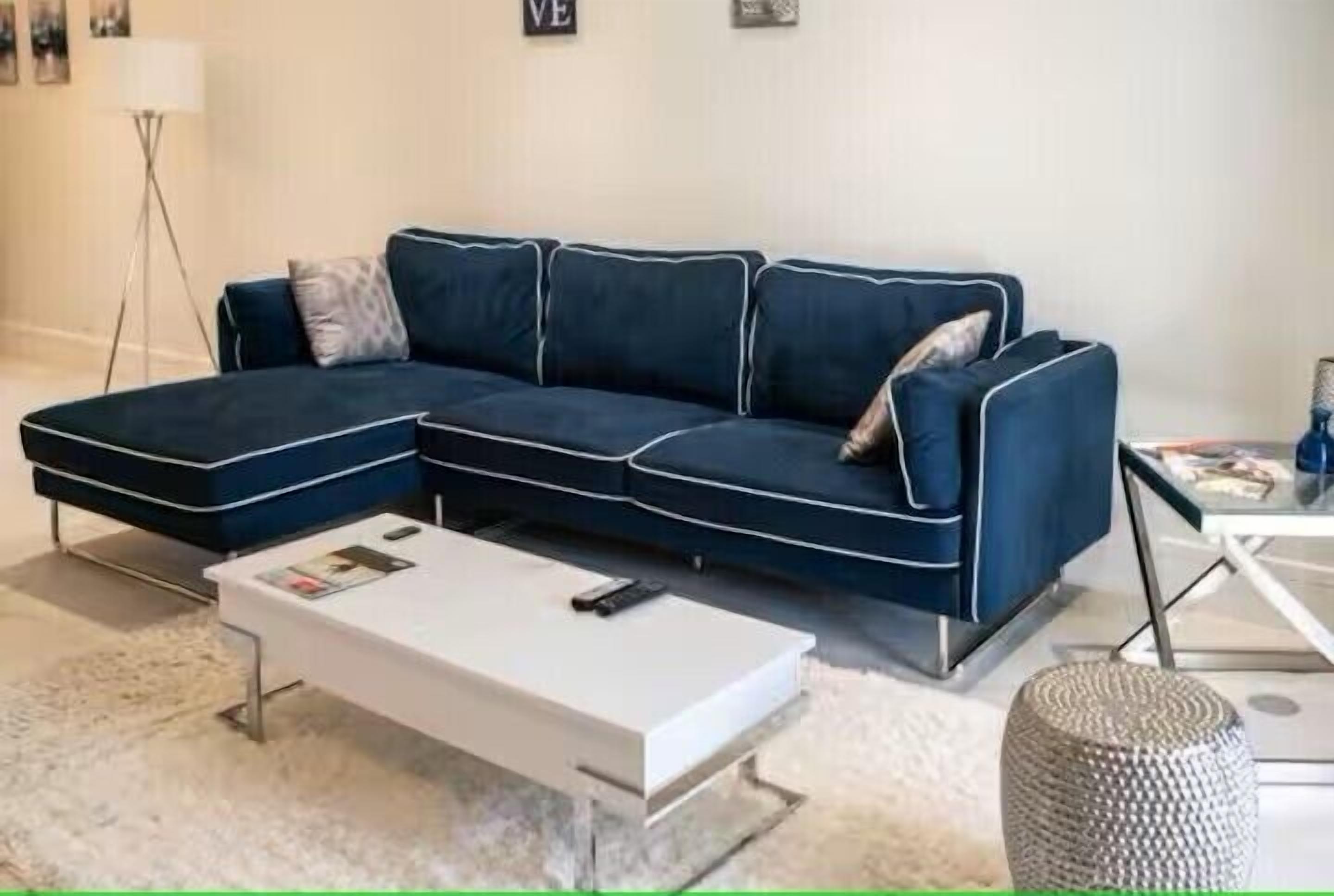 Una sala de estar moderna con un sofá seccional azul oscuro, una mesa de centro blanca y una lámpara de pie.