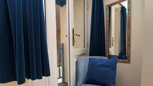 A room with a blue upholstered chair, a mirror with a floral frame, and a door leading to a balcony. - 6 Wildersmouth Court Apartments (Ilfracombe)