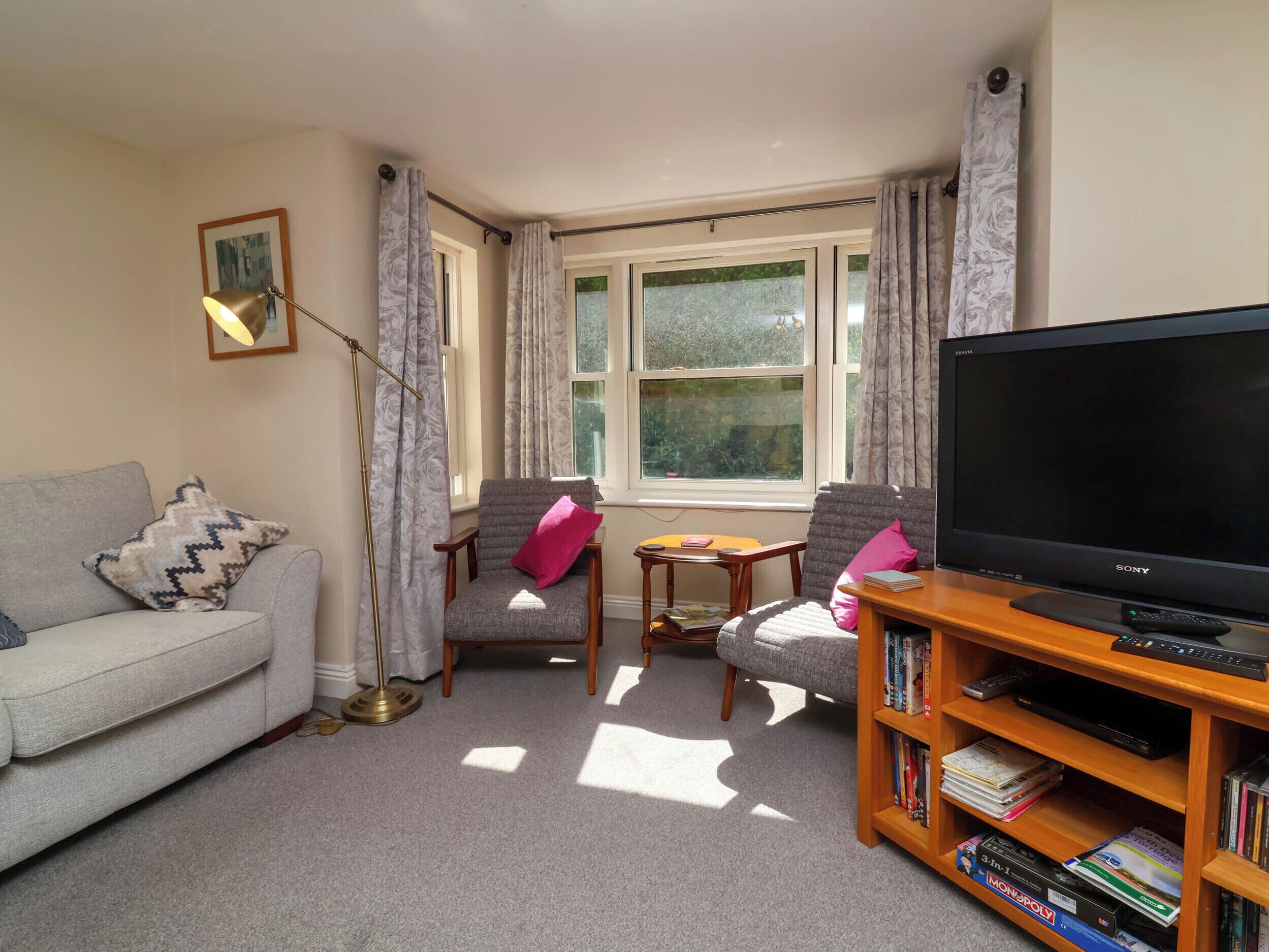 A living room with a grey sofa, two armchairs, a wooden coffee table, a bookshelf, and a large flat-screen TV.