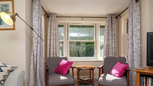 A cozy living room with two armchairs, a floor lamp, a small table, and a bookshelf. - 6 Wildersmouth Court Apartments (Ilfracombe)