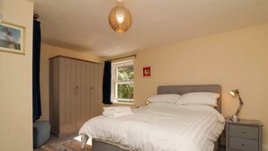 A bedroom with a bed, nightstand, wardrobe, and a hanging light fixture. - 6 Wildersmouth Court Apartments (Ilfracombe)