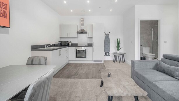 Een moderne keuken met witte kastjes, een ingebouwde oven en een hangend strijkplank.