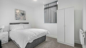 Een slaapkamer met een bed, een nachtkastje, een kledingkast en een raam met jaloezieën.