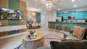 A modern living room with a TV, dining area, kitchen, and a chandelier.