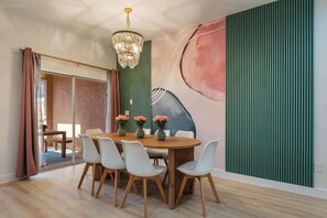 Uma sala de jantar com mesa de madeira, cadeiras brancas e flores cor-de-rosa.
