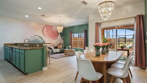 A modern kitchen with a dining area, large windows, and a chandelier.