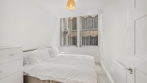 A minimalist bedroom with a bed, a dresser, a radiator, and a window with vertical blinds.