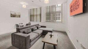 A modern living room with a sectional sofa, a small table, and a TV screen displaying "GUEST READY".