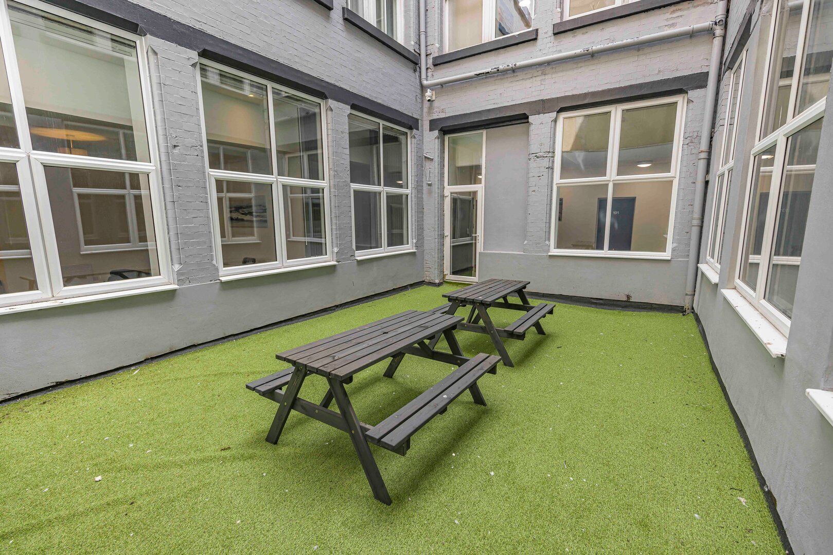 A courtyard with artificial grass and picnic tables.