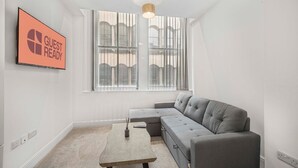 A modern, well-lit room with a grey sofa, a small table, and a 'GUEST READY' sign on the wall.