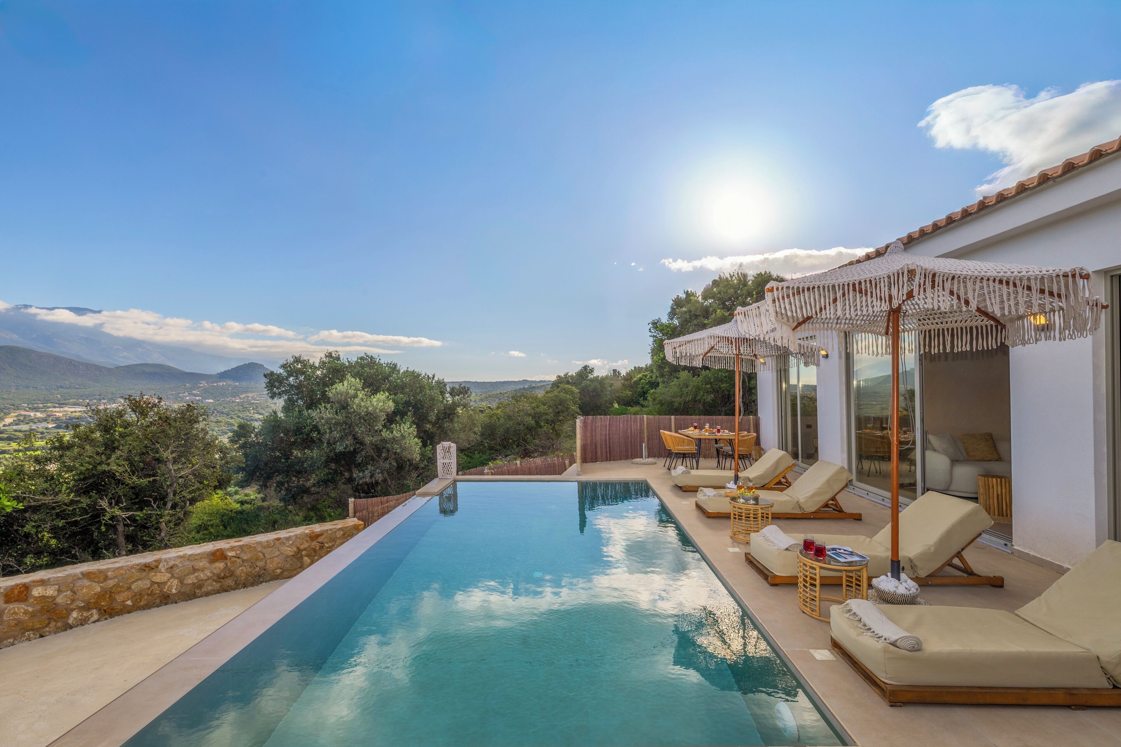 Un espace aménagé au bord de la piscine, avec des chaises longues et une table, offrant une vue sur un paysage pittoresque.
