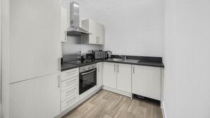 A compact kitchen with white cabinets, a black countertop, and a stainless steel range hood. - GuestReady - Relaxing retreat in Liverpool (Liverpool)