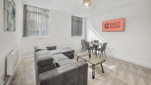 A modern living room with a grey sectional sofa, a small dining table with chairs, and a 'Guest Ready' sign on the wall. - GuestReady - Relaxing retreat in Liverpool (Liverpool)