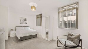 A bedroom with a bed, a chair, a wardrobe, a mirror, and a window with blinds. - GuestReady - Relaxing retreat in Liverpool (Liverpool)